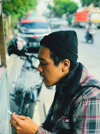 Young man looking through car on street in city