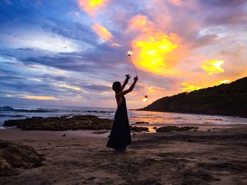 Woman standing on beach against sky during sunset