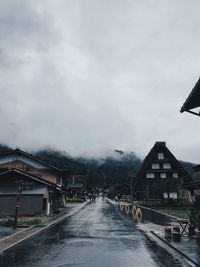 Road amidst buildings against sky during rainy season