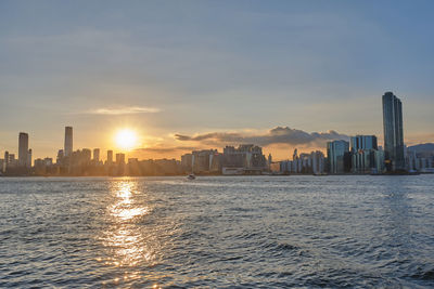 Scenic view of sea by buildings against sky during sunset