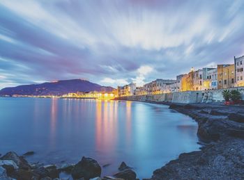 Illuminated buildings by sea against sky at dusk