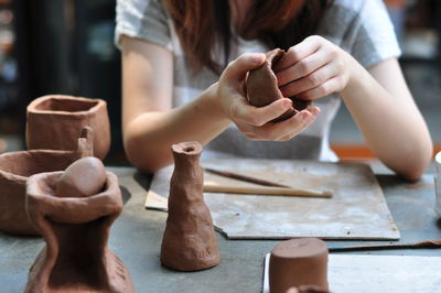 Midsection of woman making clay pots at table