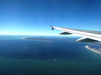 Airplane flying over sea against clear blue sky