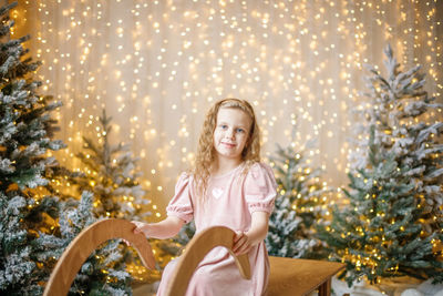 Portrait of young woman sitting against christmas tree