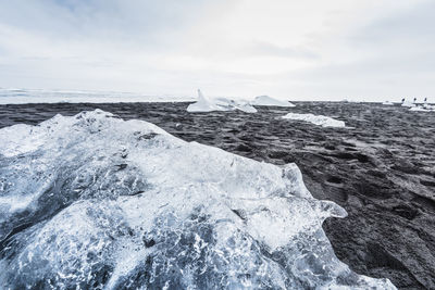 Close-up of ice over sand against sky