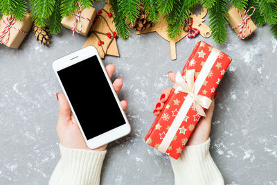 Top view of a woman holding a phone in one hand and a gift in another on cement background..