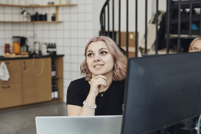 Smiling female entrepreneur with hand on chin at office during meeting