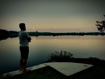 Side view of man standing by lake against sky during sunset