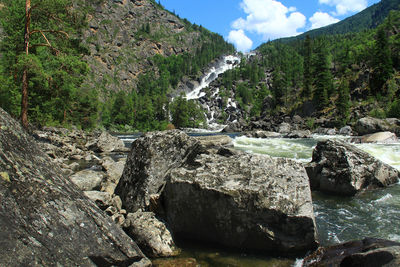 Alpine waterfall uchar in altai with huge stones and trees