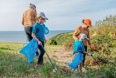 Cleanup volunteers picking up trash in garbage bags with sticks on grassy ground during environmental campaign in countryside