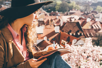 Beautiful woman in brown hat writing at the diary in view point with amazing view. 