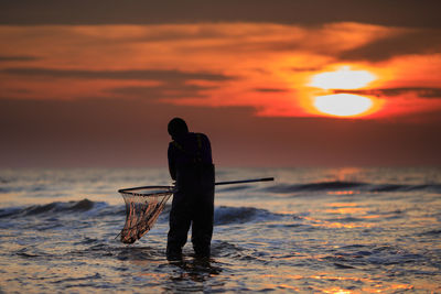 Fisherman fishing in sea during sunset