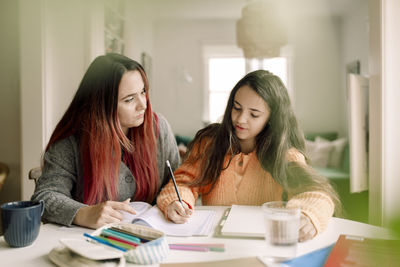 Woman assisting daughter in doing homework while sitting at table