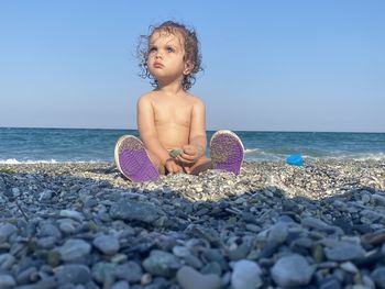 Full length of boy on pebbles at beach against clear sky