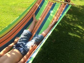 Low section of man resting on hammock over grassy field