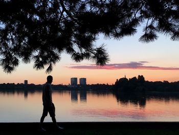 Silhouette man standing by river against sky during sunset