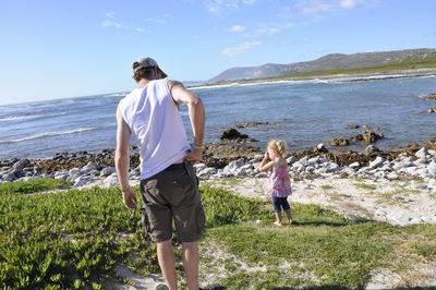 Rear view of father scratching by daughter standing by sea