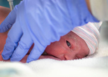 Cropped hand of doctor holding baby girl on bed