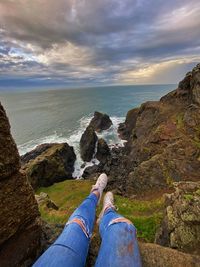 Low section of person on rock by sea against sky