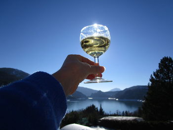 Close-up of woman holding glass against blue sky