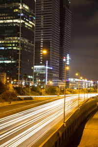 Light trails on road by buildings in city at night