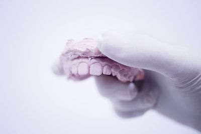 Close-up of hand holding dentures against white background
