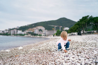 Full length of boy on pebbles at shore against sky