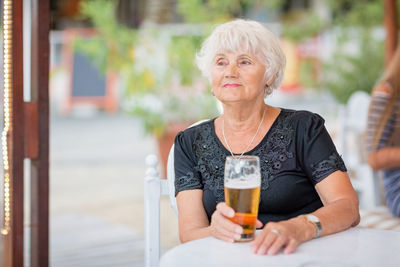 Mature woman sitting at a table in a summer cafe and drinking beer