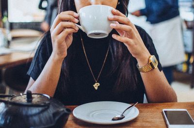 Midsection of woman drinking coffee at table in cafe