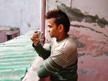 Side view of young man drinking glass against wall