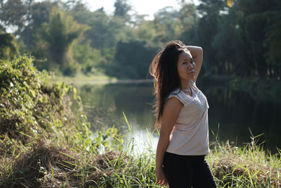 Portrait of young woman standing amidst plants against lake