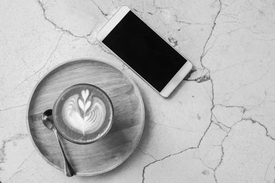 Top view hot coffee cup and smartphone with blank screen on marble table black and white concept.