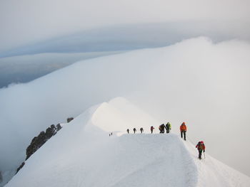 People on snow covered mountain against cloudy sky