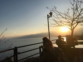 People by sea against sky during sunset