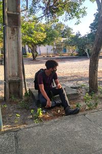 Full length of young man sitting by tree