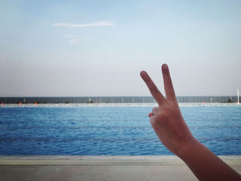 Person hand by sea against sky