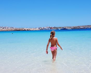 Rear view of young woman standing on beach against clear blue sky