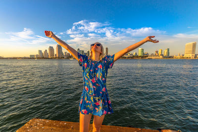 Woman with arms outstretched standing at beach in city