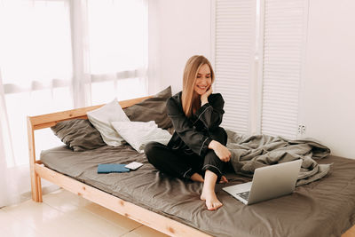 Woman using phone while relaxing on bed at home