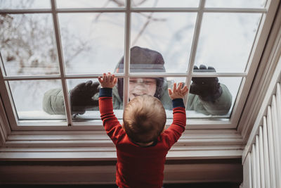 Brothers looking at each other through window in the winter with snow