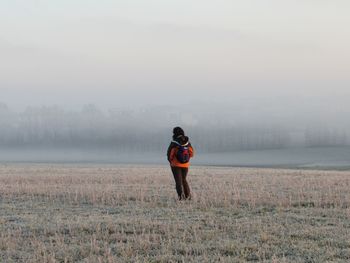 Rear view of woman standing on field against foggy weather