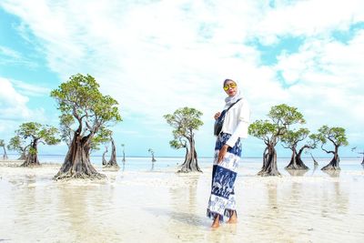 Person standing by tree on beach against sky