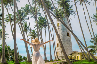 Rear view of woman with arms outstretched standing against trees