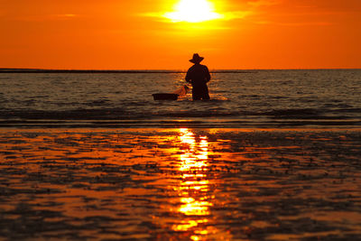Silhouette man standing on sea against orange sky
