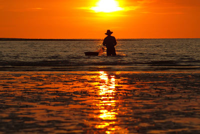 Silhouette man fishing in sea against orange sky