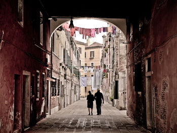 Rear view of woman and man walking in alley amidst buildings