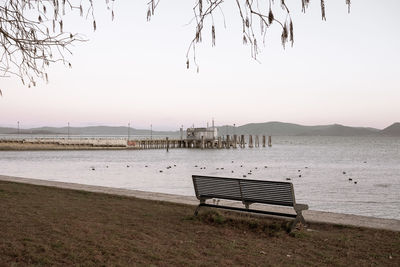 Empty bench on beach against clear sky