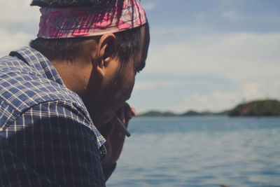 Side view of man smoking cigarette by sea against sky