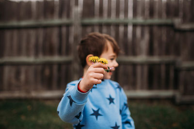 Young boy wearing blue sweatshirt holding yellow flowers outside