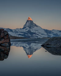 Reflection of matterhorn mountain in lake against clear sky during sunset